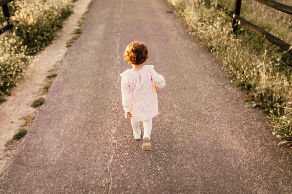 brown-haired little girl in white walking down road alone