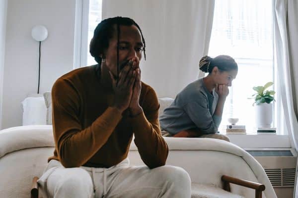 man and woman sitting apart and upset on a bed