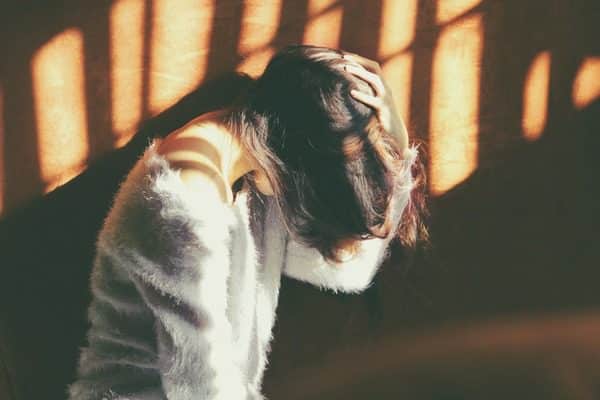 brown haired woman in gay sweater holding her bowed head