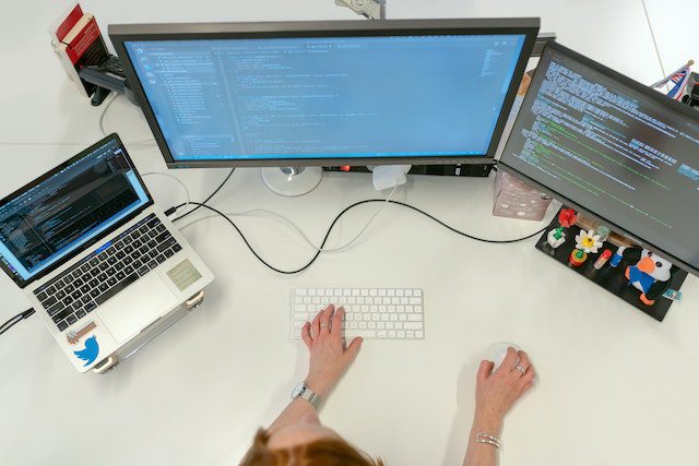 womans hands as she works three computers